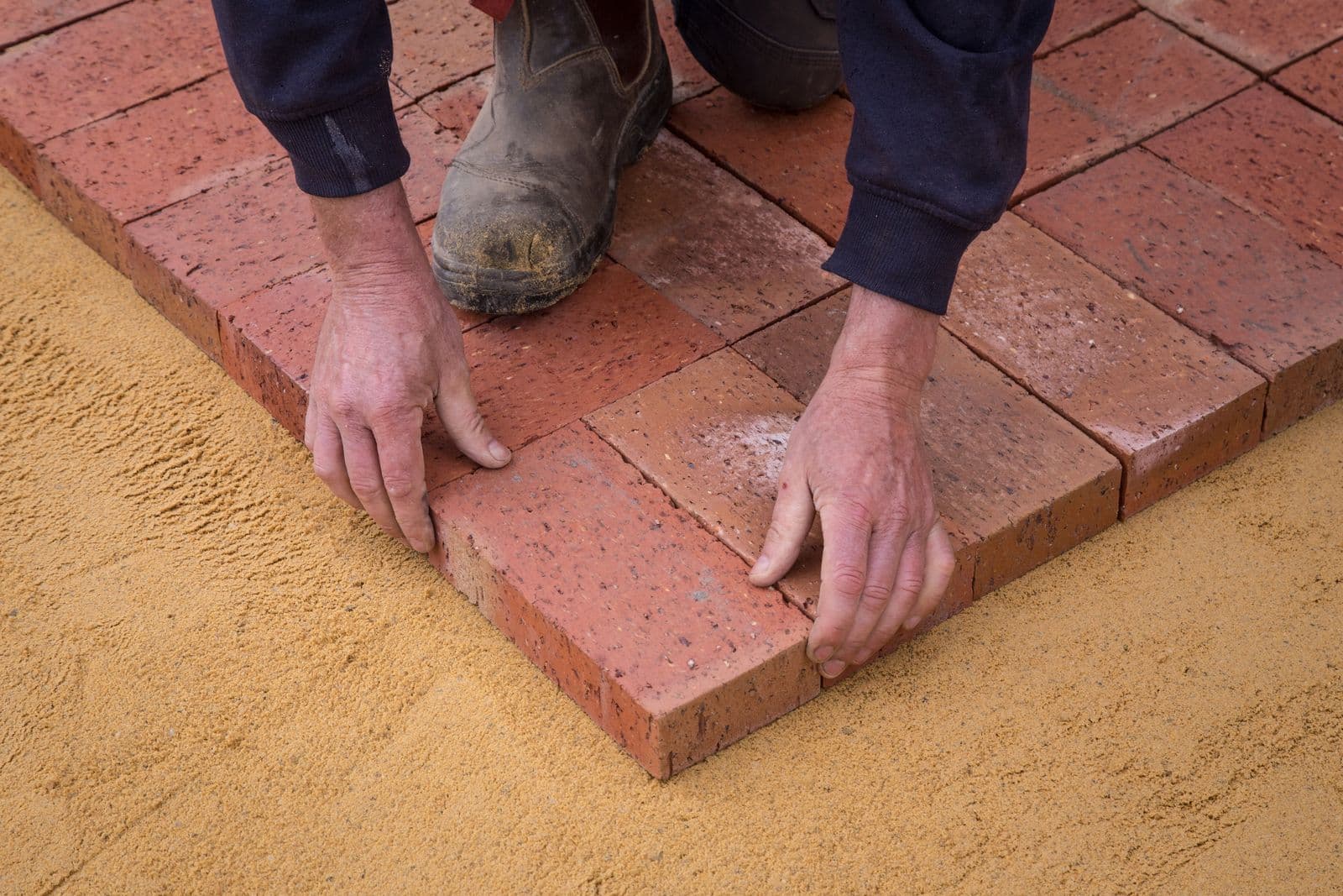 Setting clay pavers by hand on a screeded sand bed